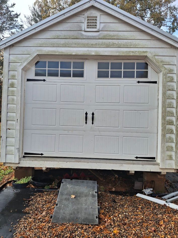 White garage door with windows, black hardware, and ramp, on a wood shed.