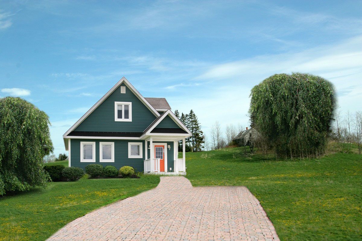 Green house with stone walkway on a grassy lawn under a blue sky.