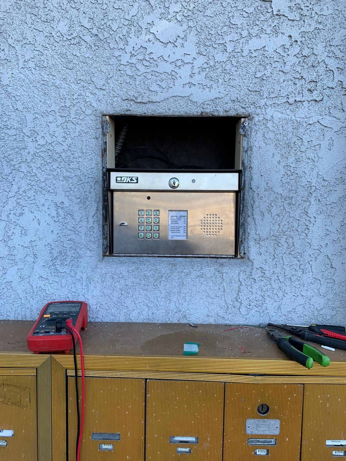 Mailboxes with a meter resting on the ledge and electrical wires connected to the mailbox panel.