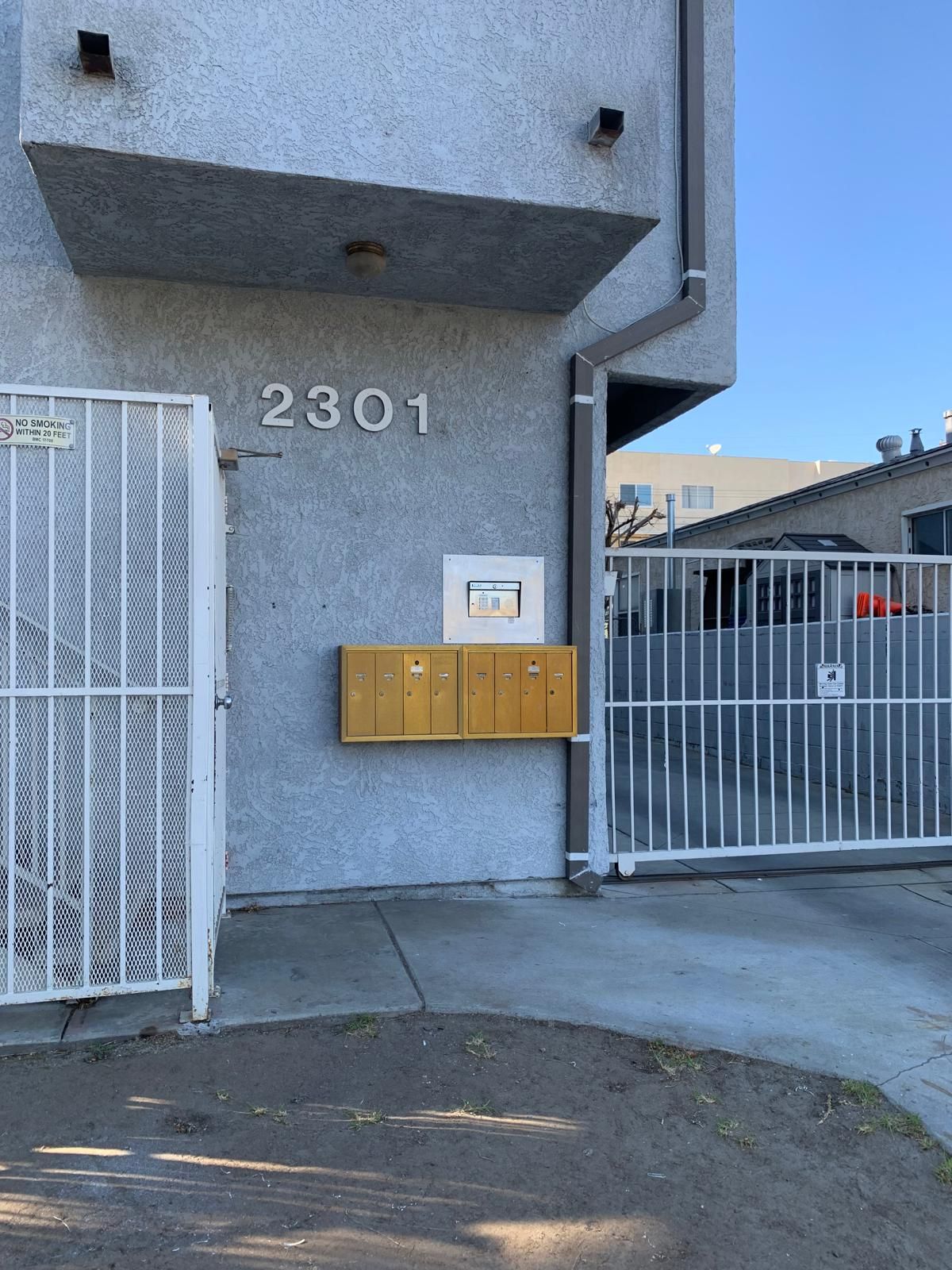 Exterior view of apartment building at 2301, with a gated entrance, mailbox, and a light blue sky.