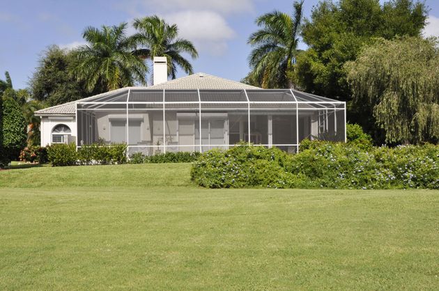 Screened white house or patio enclosure amid lush green lawn and tropical trees