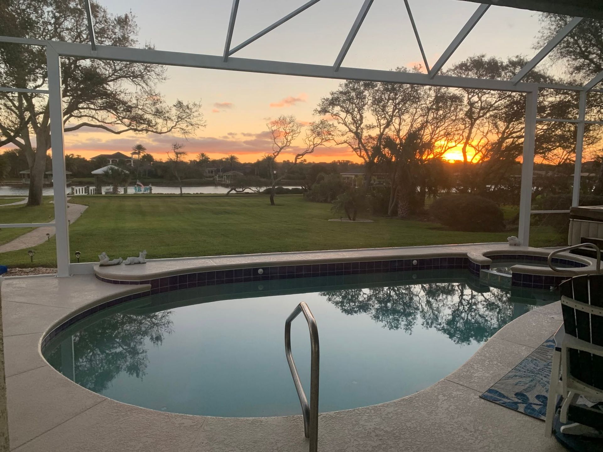 Backyard pool at sunset with screened enclosure, palm trees, and glowing orange sky