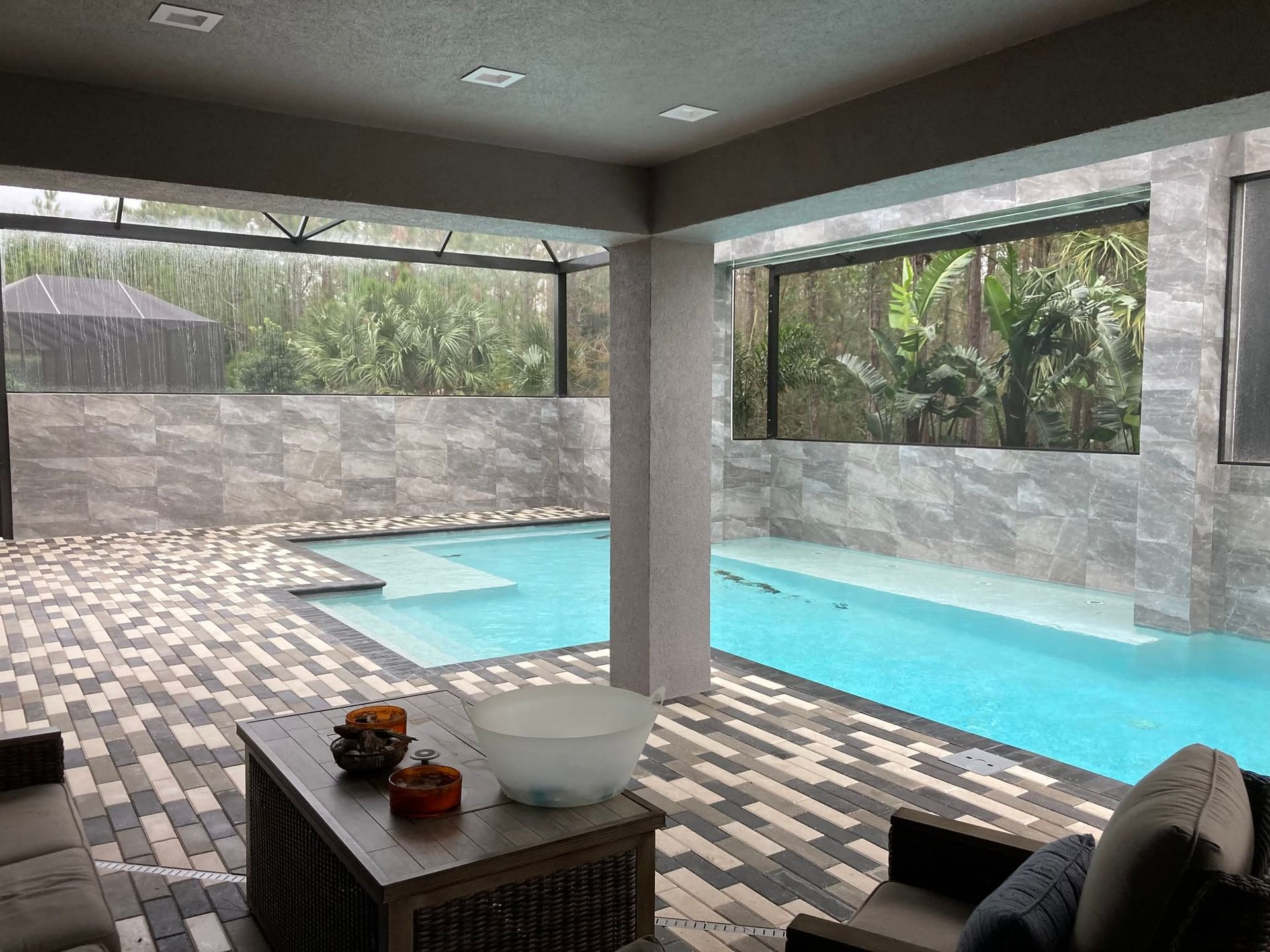 Covered patio with a turquoise pool, gray stone walls, and outdoor seating area