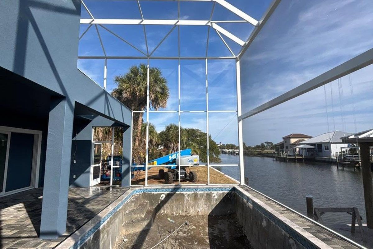 Waterfront patio under construction with blue tarps, white framing, and a canal view on a sunny day