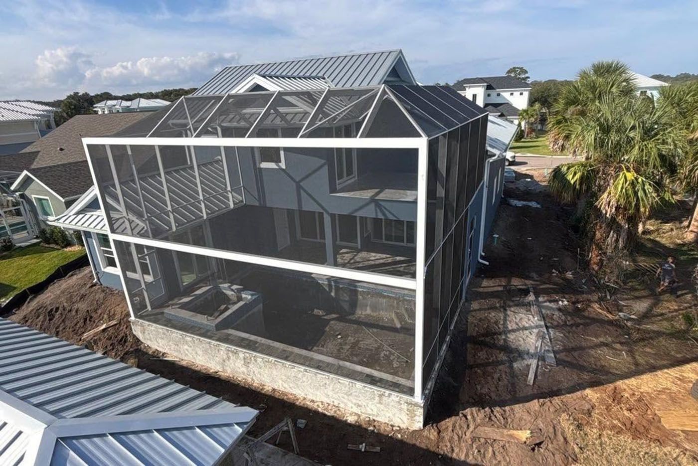 Large screened-in house structure with gray roof in a suburban area under construction