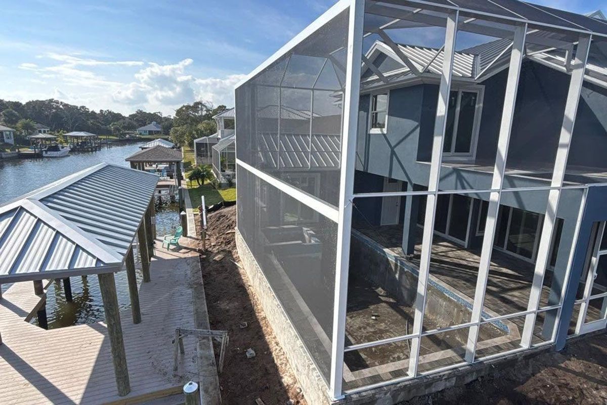 Modern house exterior with screened-in patio beside a walkway and blue metal roof, overlooking a waterfront