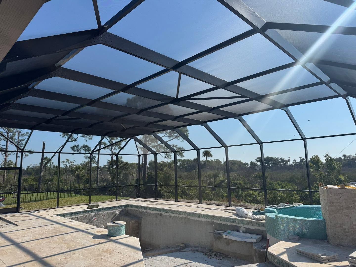 Covered outdoor patio with screened roof, concrete bar, and poolside view of trees beyond the enclosure