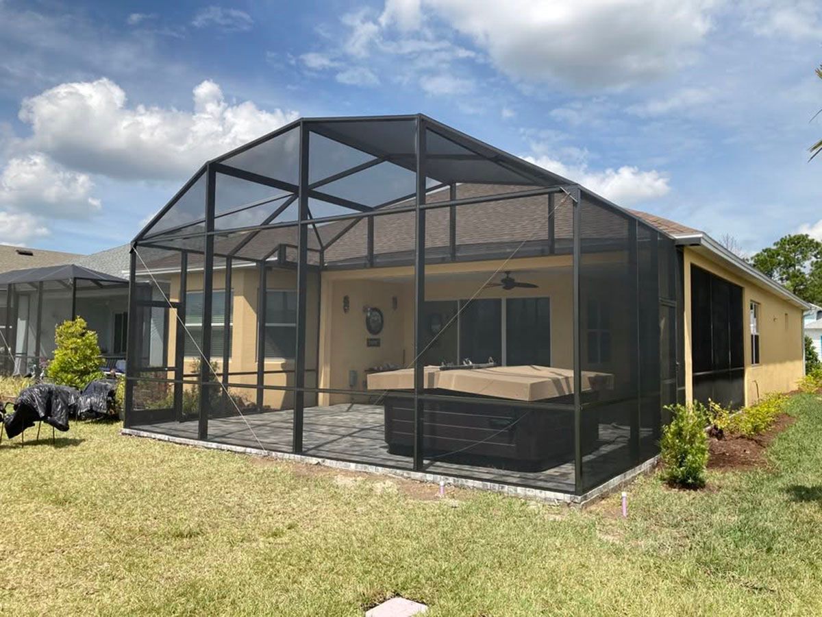 Screened patio enclosure attached to a tan house with a dark roof under a cloudy sky