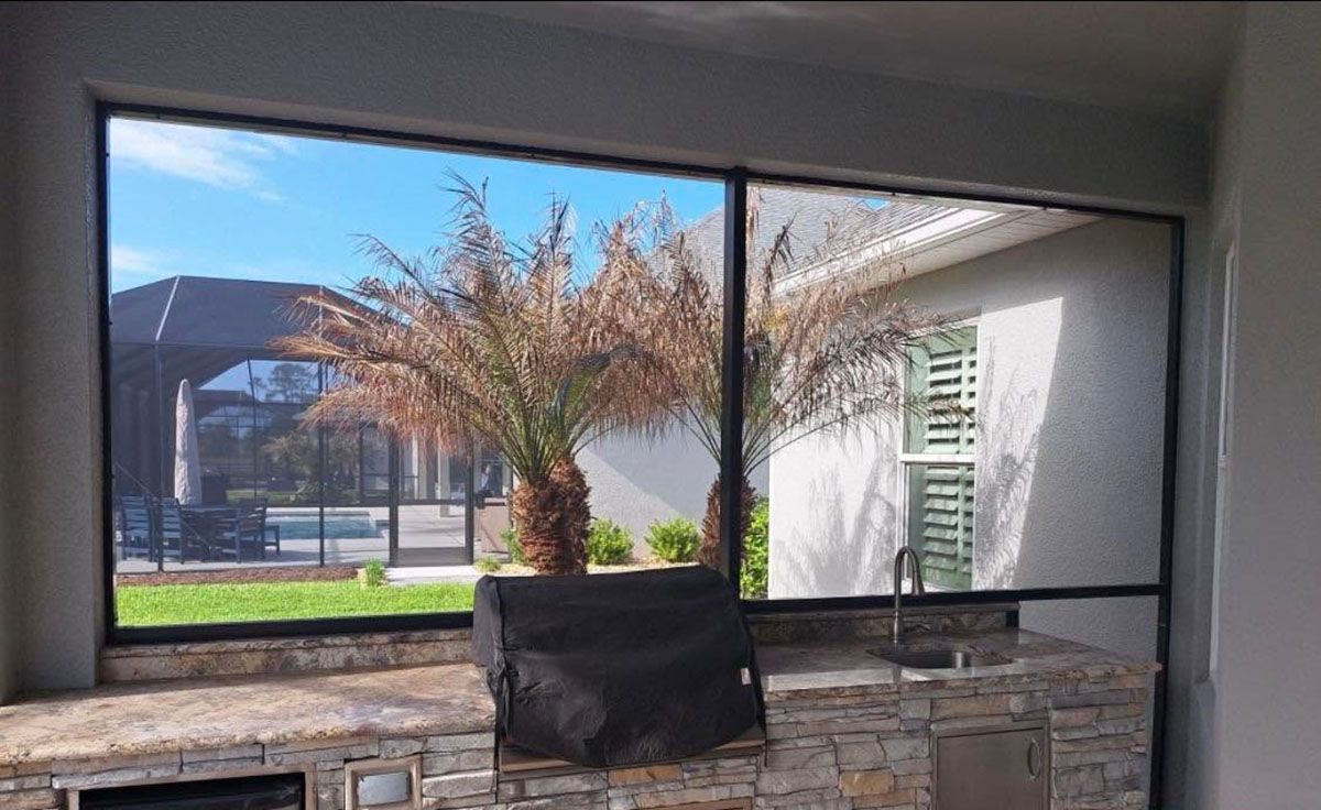 Patio with stone wall, black chair, and window view of a palm tree and sunny courtyard