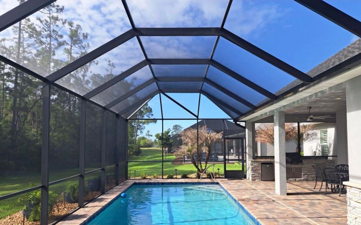 Screened-in backyard pool with blue water, patio seating, and a view of the lawn and trees
