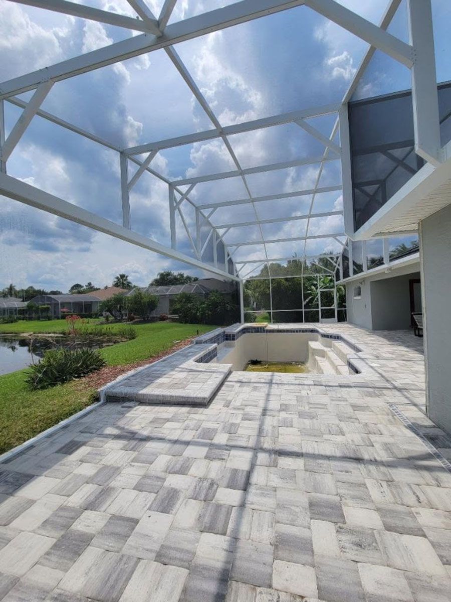Covered stone patio with pool, glass railing, and landscaped garden under a cloudy sky