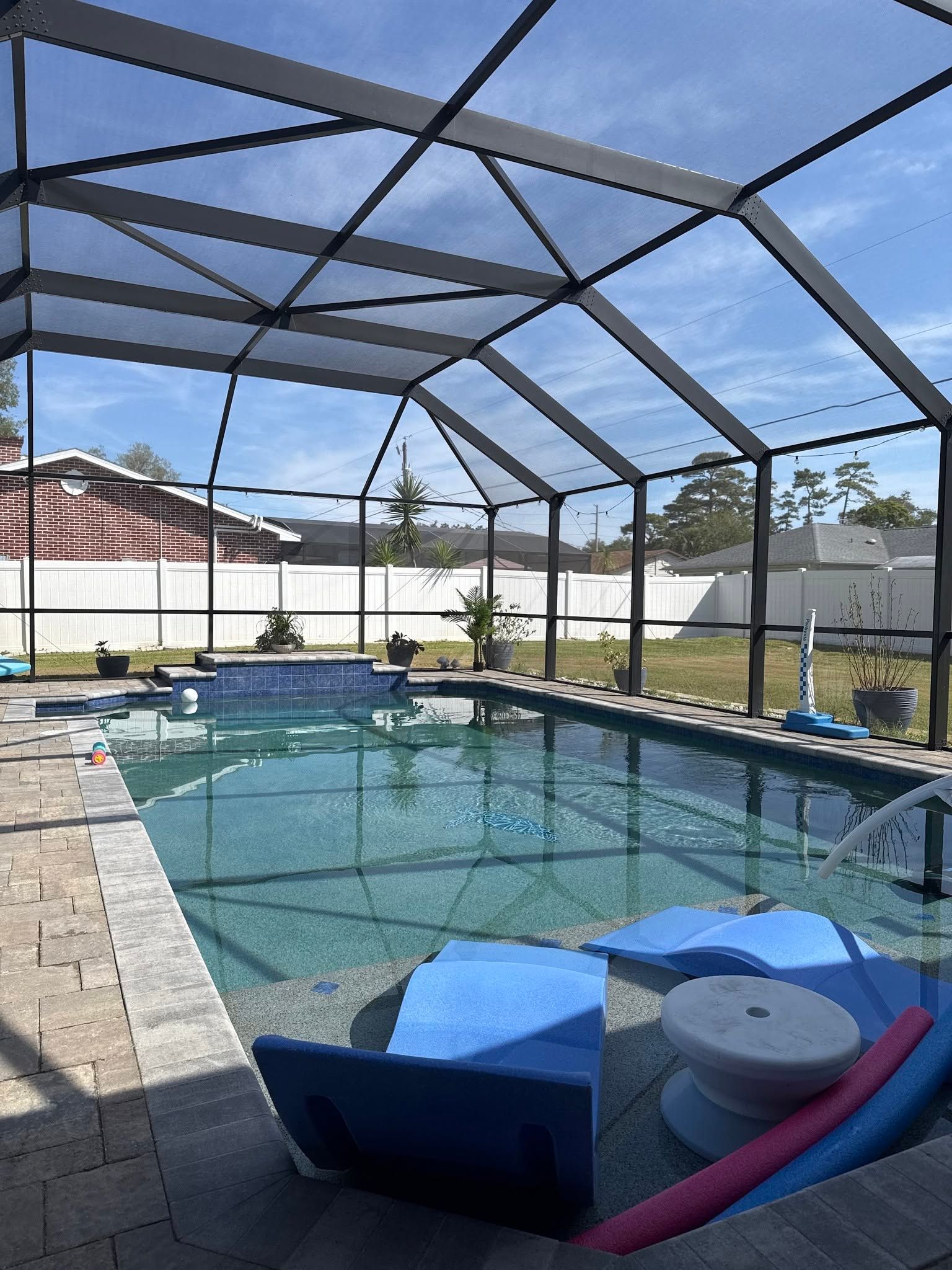Screened-in backyard pool with clear blue water, patio chairs, and a sunny sky.