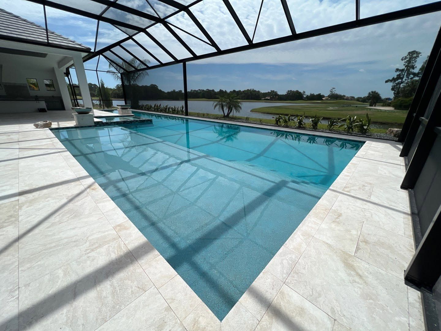 Covered outdoor swimming pool with blue water, screened enclosure, and lake view beyond