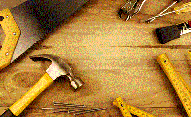 Assortment of carpentry tools: hammer, saw, measuring tape, pliers, and screwdriver on a wooden surface.