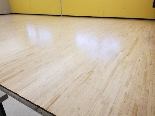 Wooden gymnasium floor, reflecting overhead lighting; yellow wall in background.