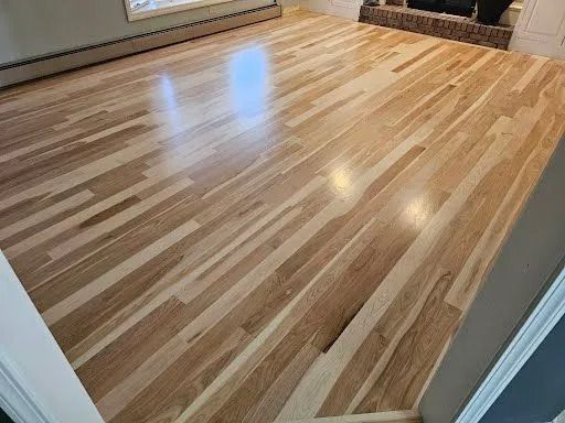 Hardwood floor, medium-toned, with sunlight reflection, in a room, with hints of wall and trim.