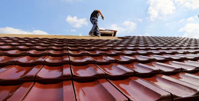A house with a shingle roof and dormer windows under a blue sky.