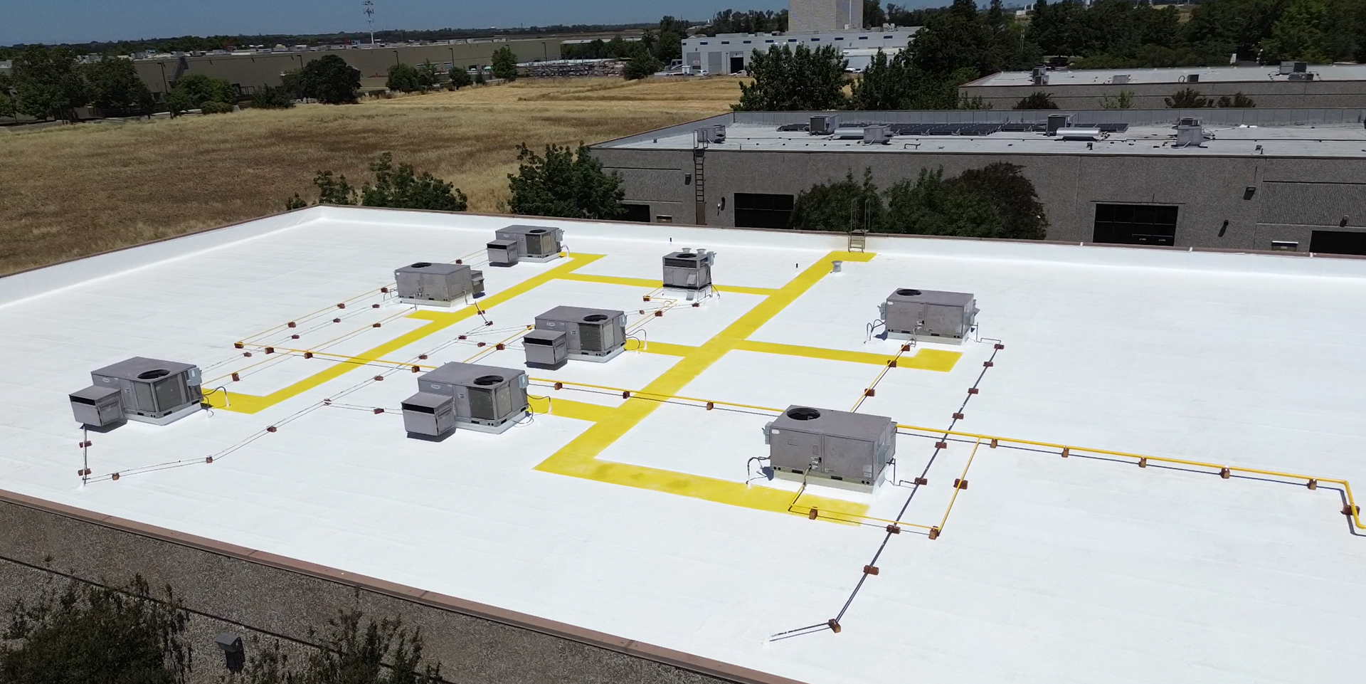 An aerial view of a white commercial roof with multiple HVAC units and bright yellow painted safety walkways.