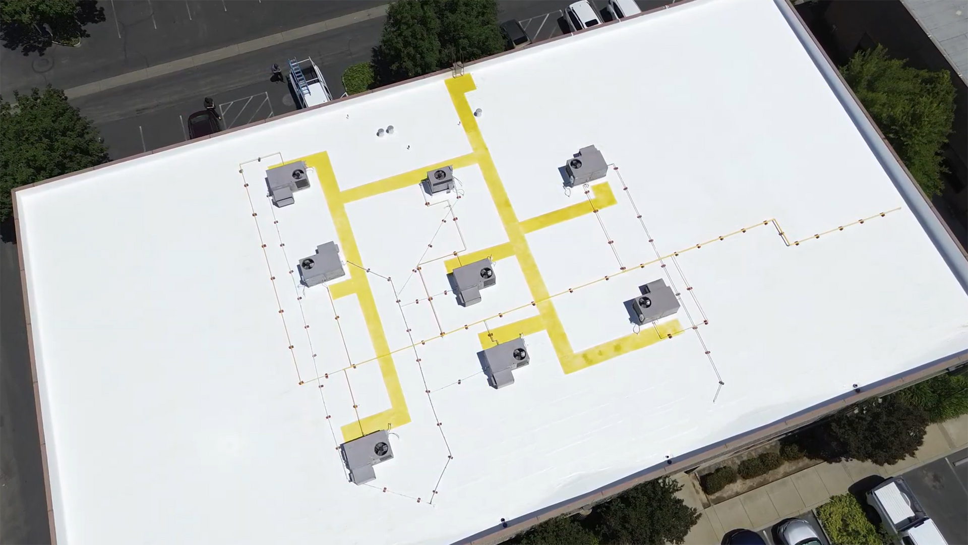 Aerial view of a white flat roof with yellow utility lines connecting several HVAC units.