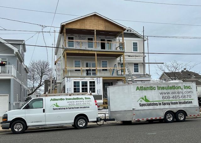 A two-story house under construction with a trailer and van from Atlantic Insulation, Inc. parked in front.