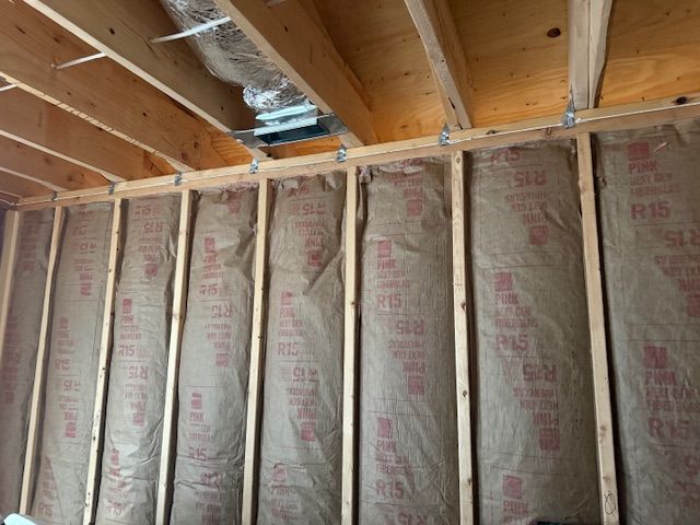Interior wall with insulation between wooden studs, and ductwork visible in the ceiling.