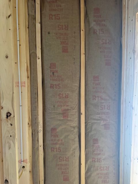 Wooden wall framing with R15 insulation installed between studs, with electrical wire visible.