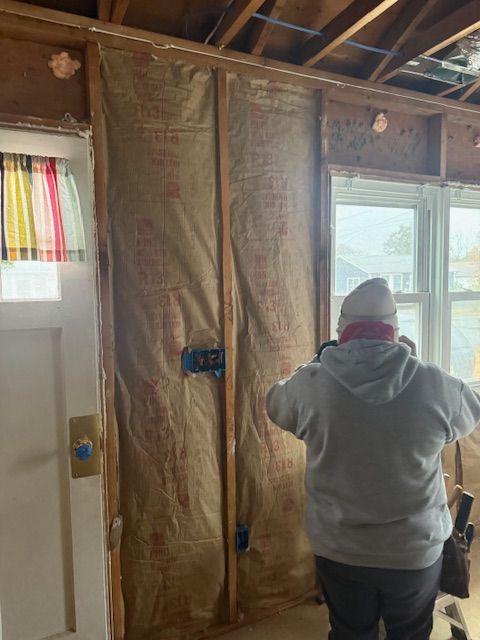Person installing insulation in a wall, with visible electrical boxes. Interior view.