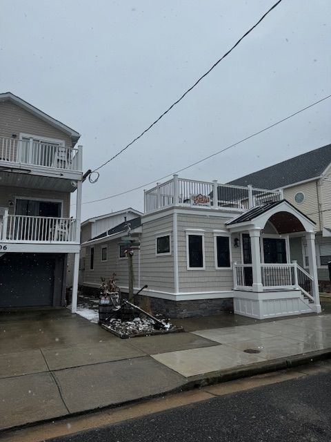 Coastal houses on a grey day. Light-colored siding, rooftop deck, and porch. Snow or sleet on the ground.