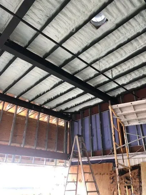 Interior construction with black beams, white insulation, partially built walls, and a skylight.
