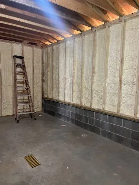 Interior view of a room with spray foam insulation on the walls and ceiling. A ladder is present.