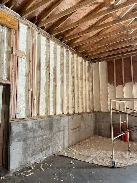 Interior wall partially insulated with spray foam in a room with wood framing and concrete foundation.