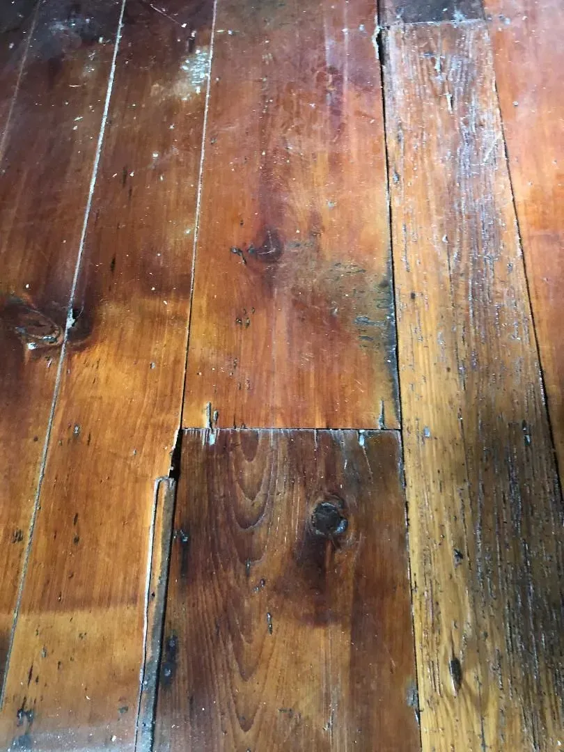 Close-up of worn wooden floorboards with cracks and discoloration; a rustic, aged appearance.