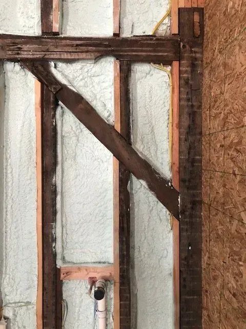 Interior wall framing with spray foam insulation. Diagonal beam, electrical wire visible. Right side is plywood.