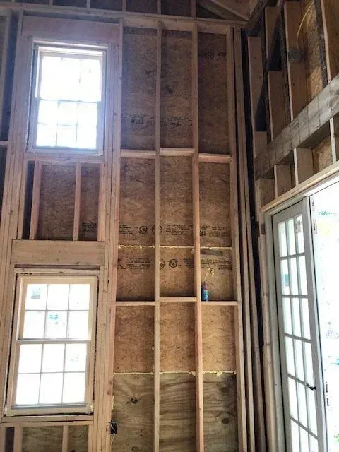 Interior wood framing for a wall with two windows and a door, under construction.