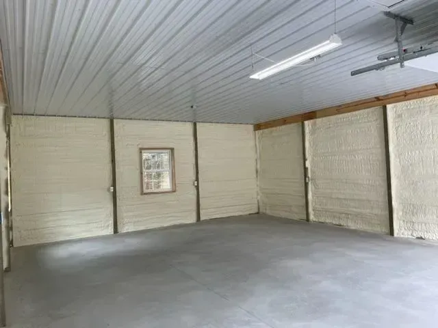 Interior of a garage with spray foam insulation on the walls. Gray concrete floor and white ceiling.