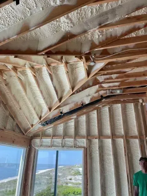 Interior view of a building under construction, showing spray foam insulation between wooden rafters and studs.