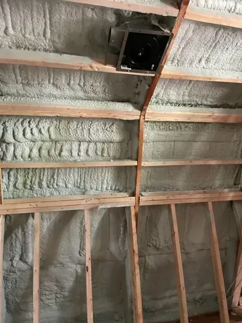 Interior of a wooden structure insulated with spray foam. A ventilation fan is mounted in the ceiling.