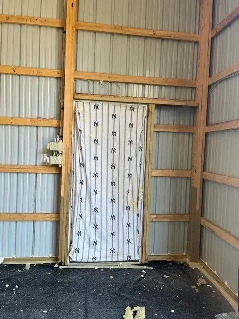 Interior of a barn with metal walls, wooden beams, a framed doorway, and a hanging curtain.