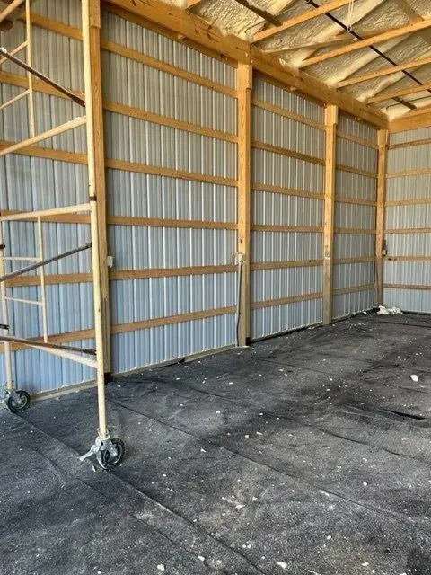 Interior of a pole barn with metal siding, wooden beams, and black flooring.