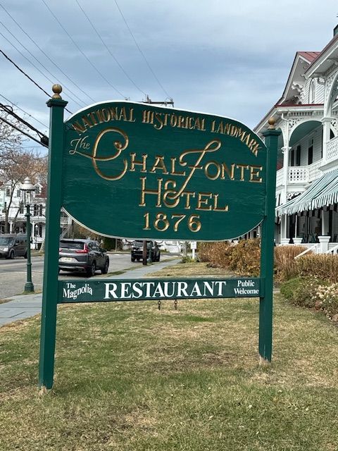 Green sign for The Chalfonte Hotel, a National Historical Landmark, with gold lettering. Grass and road in foreground.