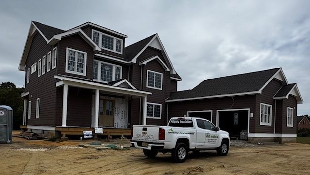 Brown two-story house under construction with a white pickup truck parked in front. Cloudy sky overhead.