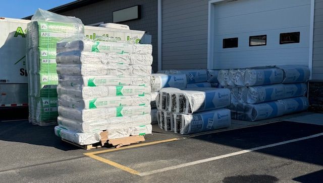 Pallets of packaged building insulation outside a commercial building with a loading dock.