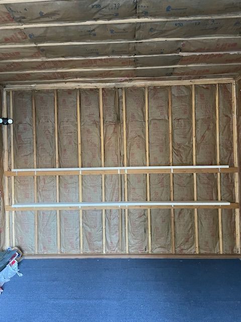 Interior view of a framed wall and ceiling with insulation installed, two horizontal boards, and a blue floor.