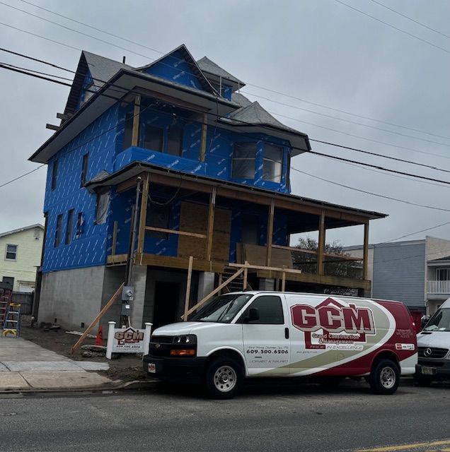 House under construction with blue wrap, GCM van parked in front.