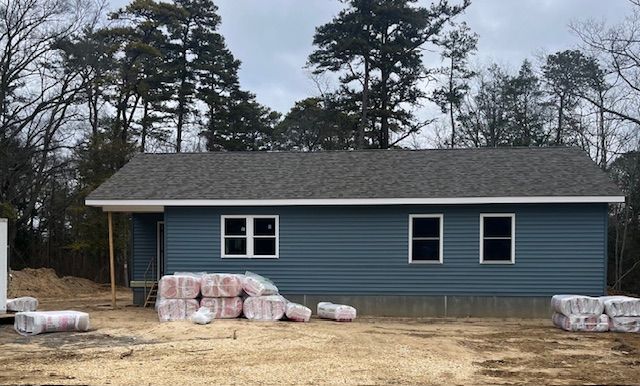 Blue house under construction with building materials in front; trees in the background.