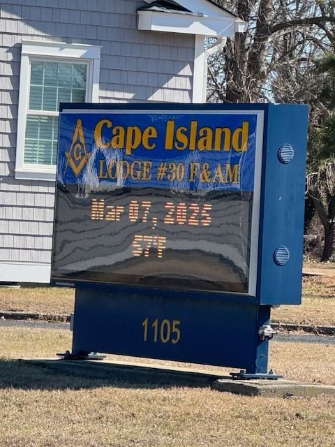 Cape Island Lodge sign with date Mar 07, 2025, and temperature 57°F. Building in background, blue sign, yellow text.