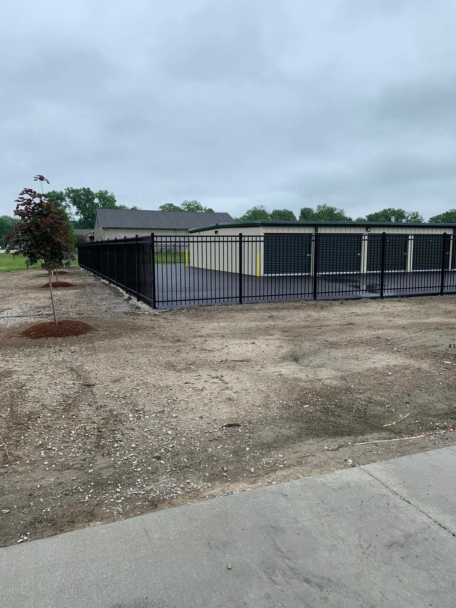 A black metal fence encloses a long, multi-unit storage building on a grey, overcast day.