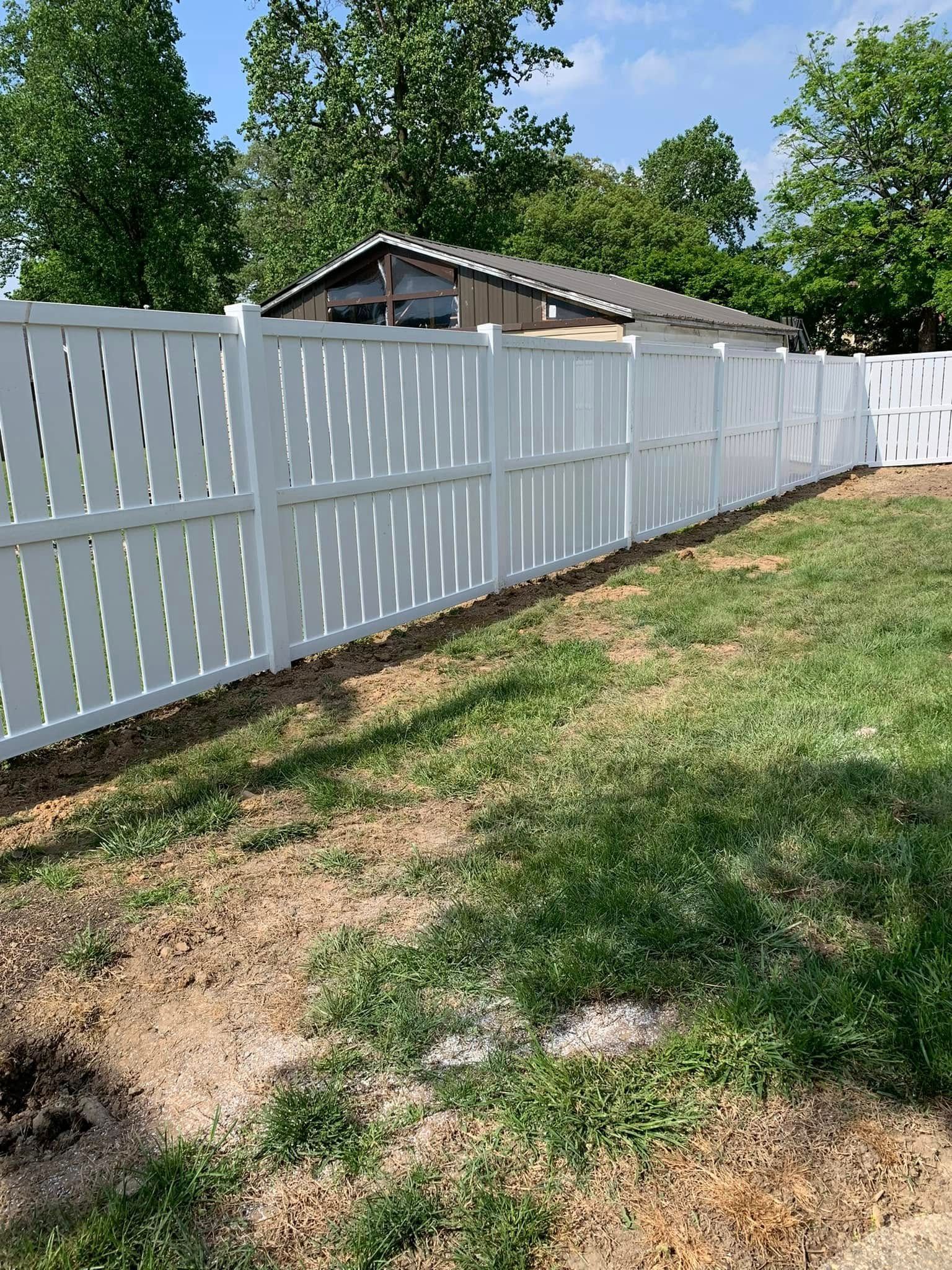 A long white vinyl privacy fence stands in a backyard with a grassy lawn and a shed in the background.
