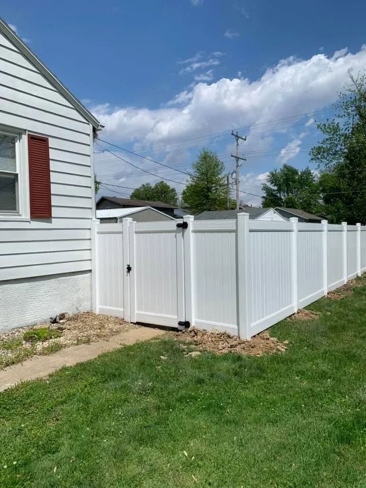 A side view of a white vinyl privacy fence with a closed gate next to the white siding of a house.