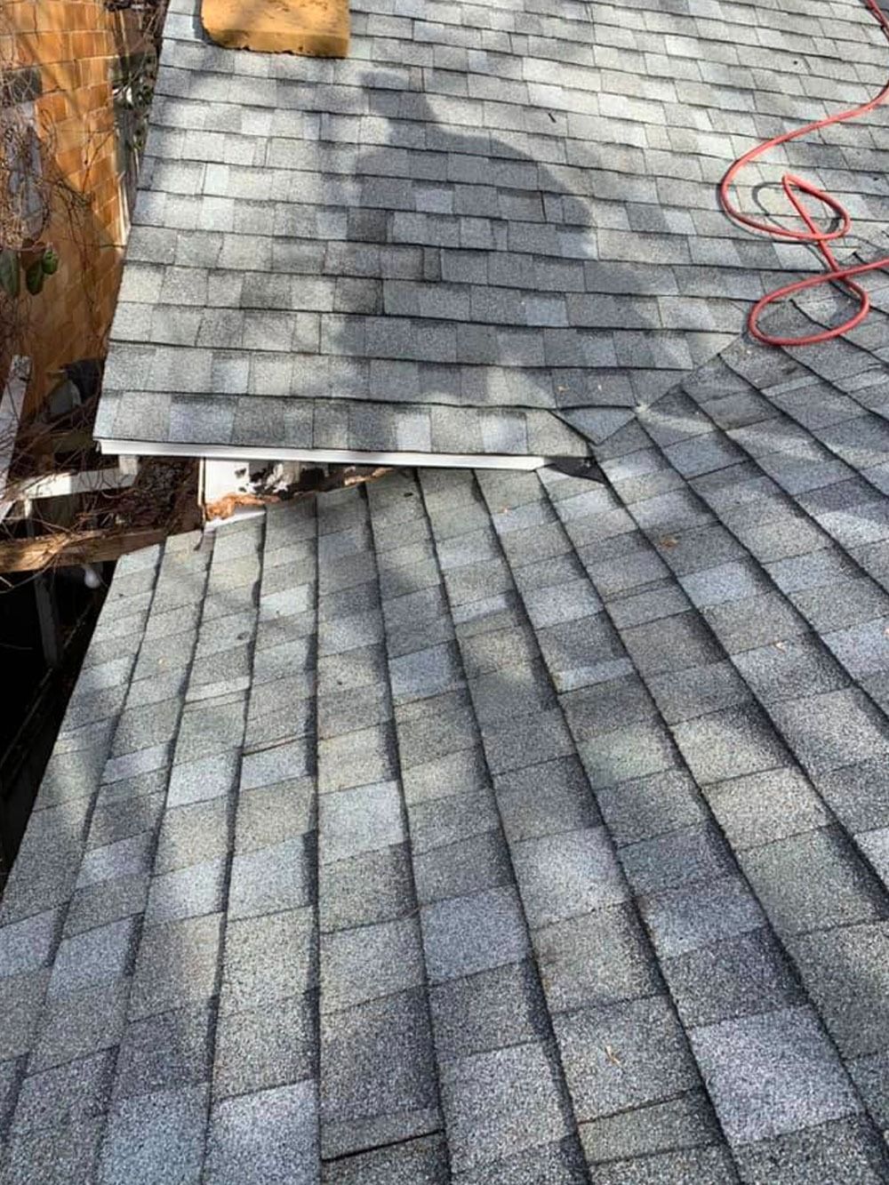 A view from above showing a grey shingled roof with a shadow, a gutter section, and a red cord coiled on the shingles.